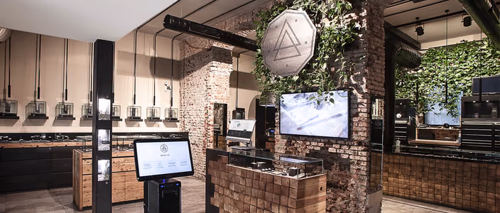 Inside a Nove25 store: exposed brick, wooden counters with display cases, a wall of ivy and a touch-screen kiosk.