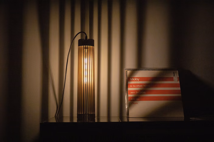A Shapelamp pendant light with vertical ribbed design illuminated next to a CD case for scale reference
