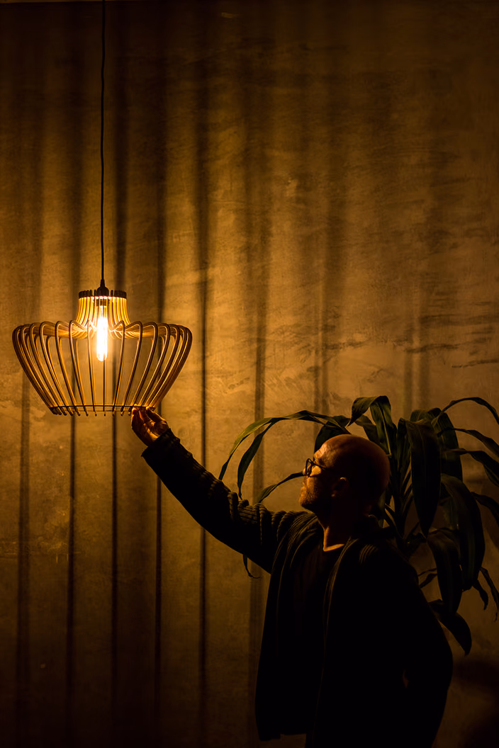 A person reaching to hold a lit Shapelamp pendant, demonstrating installation and the striking shadows it creates on the wall