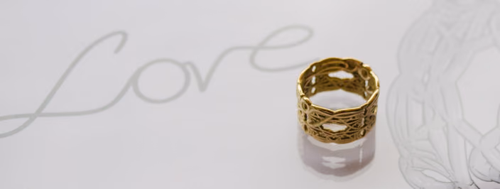 Gold ring from the Signature Collection featuring organic flowing patterns with hand-drawn curves in the background.