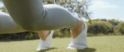 Close-up of feet in white, perforated Vivobarefoot shoes, bending on a lawn