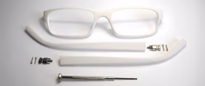 A white 3D-printed eyeglass frame laid out in parts: the front, two temples, hinges, and screws, next to a small screwdriver